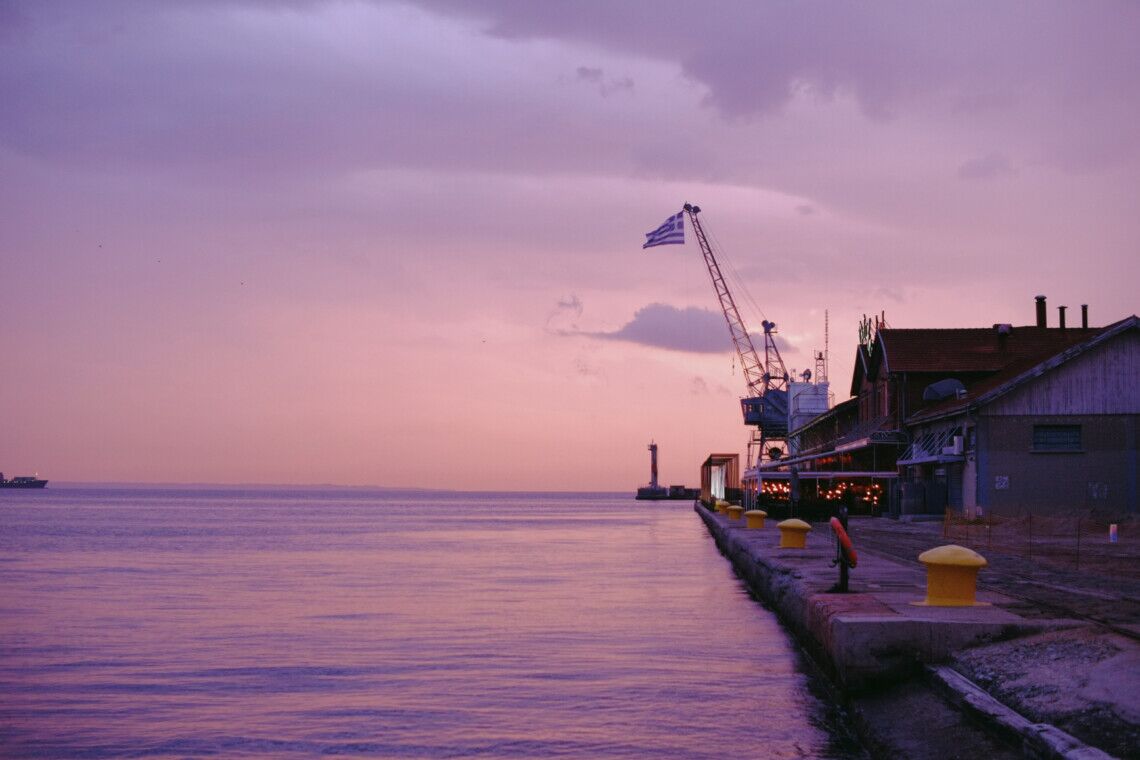 Old Port of Thessaloniki at sunset with Greek flag and dockside buildings